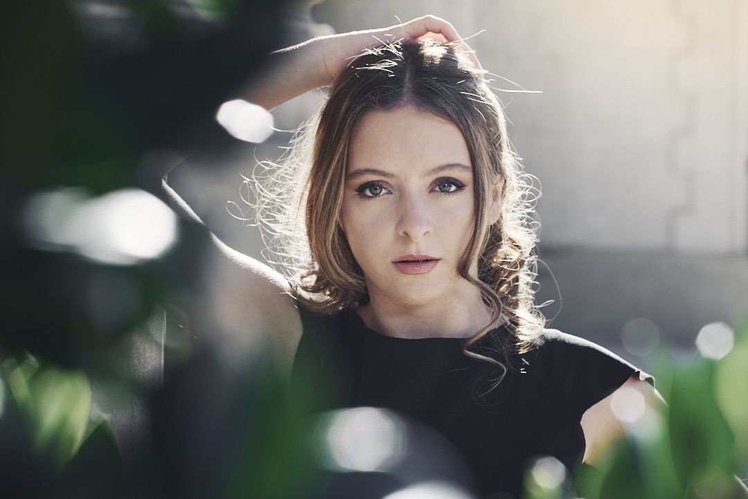 Foto editorial de 15 con luz suave atravesando follaje, estética artística y mirada protagonista; tendencia premium en Yerba Buena. Book de 15 años.